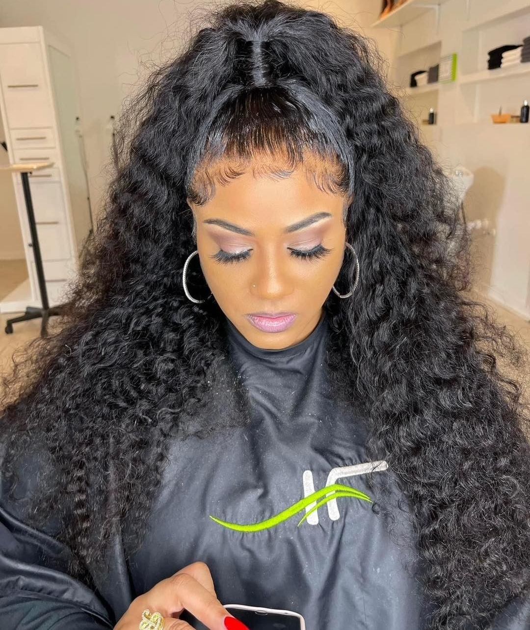 Woman with curly hair and makeup looking down, wearing black top