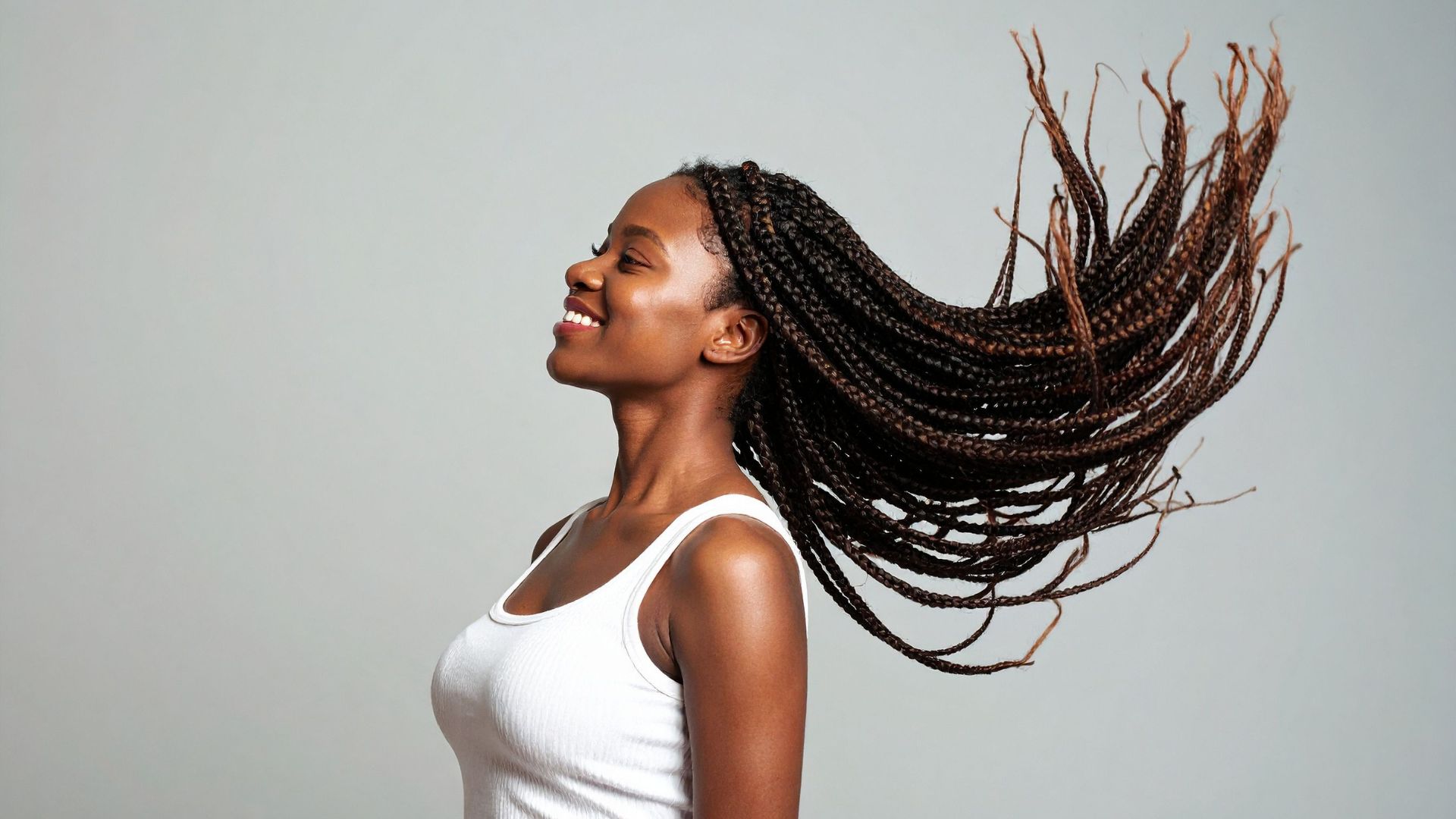 Woman with braids flipping hair with joy against gray background